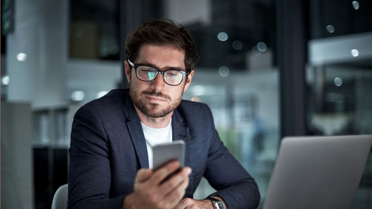 A businessman looking at his phone while sitting at his desk.