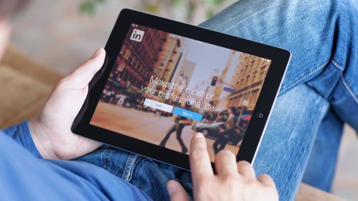 A man is sitting on a couch with a tablet displaying linkedin.