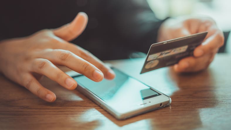 A person is holding a credit card while using a smartphone.