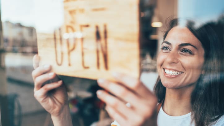 A woman holding up an open sign in front of a shop window.