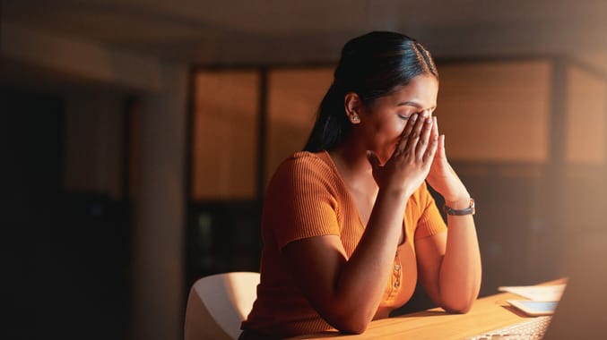 A woman covering her face while sitting at a desk.