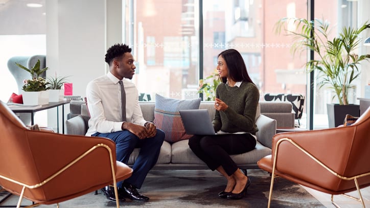 Two business people sitting on a couch in an office.