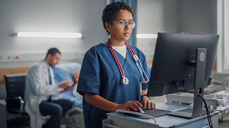 A nurse is working on a computer in a hospital room.