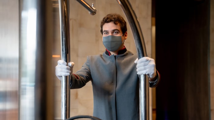 A man in a mask is holding luggage in a hotel.