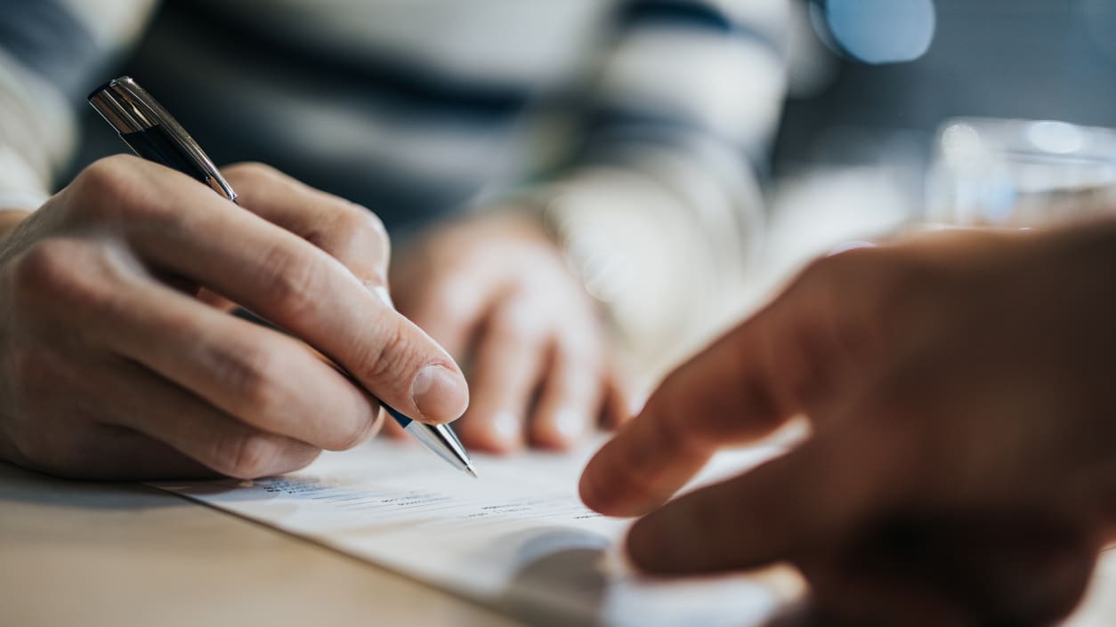 A person signing a document with a pen.