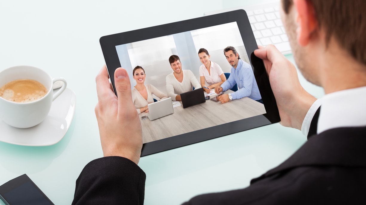 A man in a business suit is using a tablet to watch a video conference.