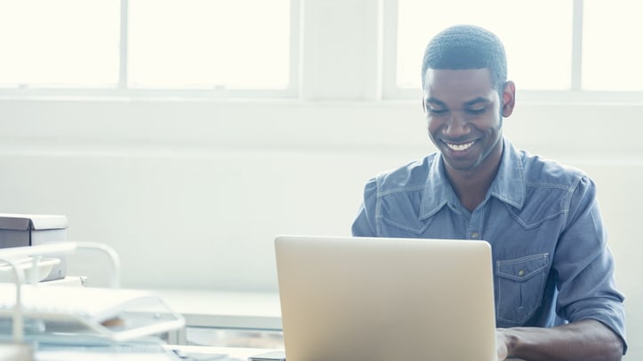 A smiling man using a laptop in his office.