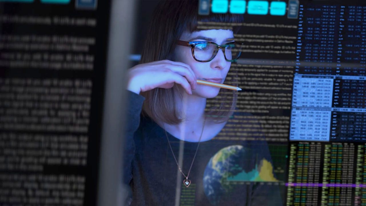 A woman in glasses is looking at a computer screen.