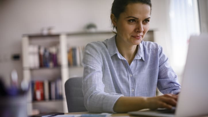 A woman is sitting at a desk using a laptop.