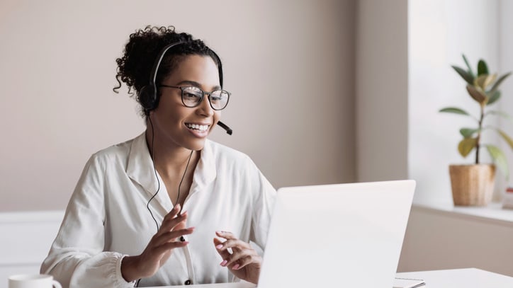 A woman wearing a headset and working on a laptop.