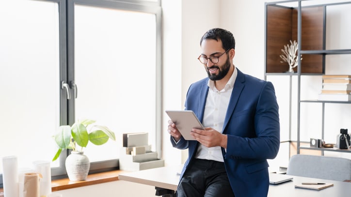 A businessman in a suit is using a tablet in his office.