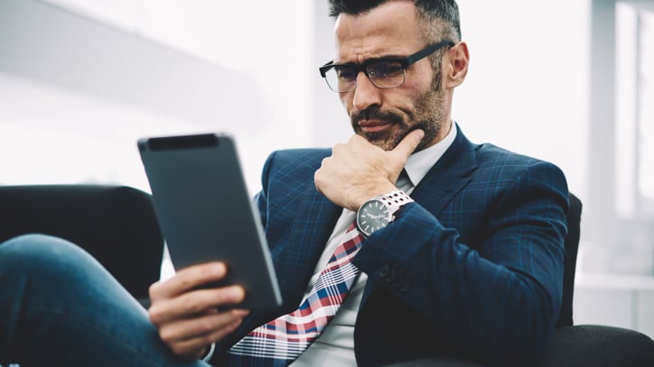 A businessman looking at a tablet while sitting in a chair.