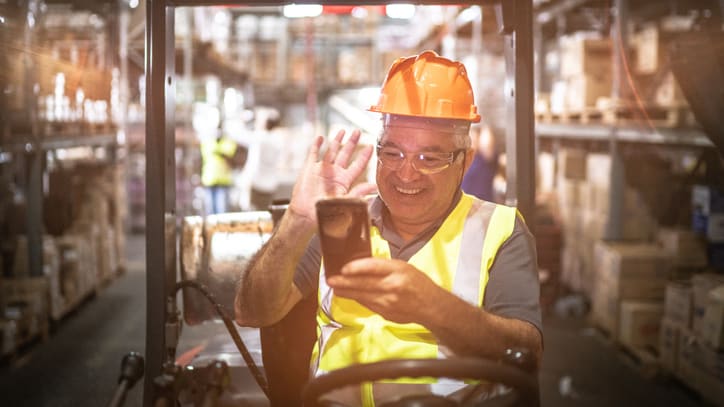 A man in a hard hat driving a forklift in a warehouse.
