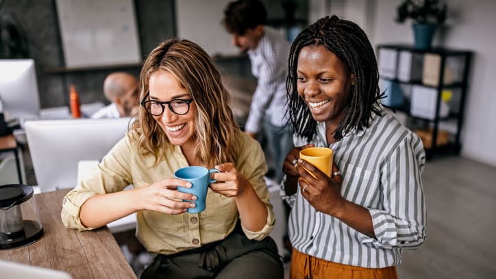 Two women drinking coffee in an office.