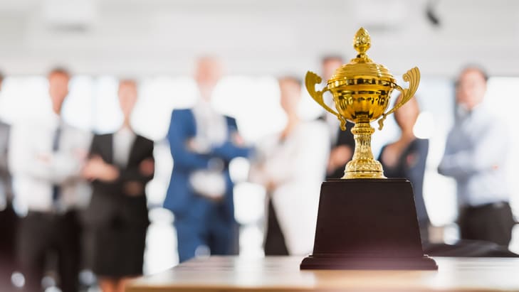 A golden trophy on a table in front of a group of people.