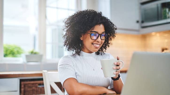 A woman in glasses is working on her laptop while drinking a cup of coffee.