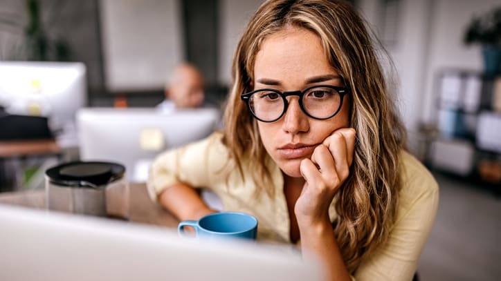 A woman in glasses sitting at a desk with a cup of coffee.