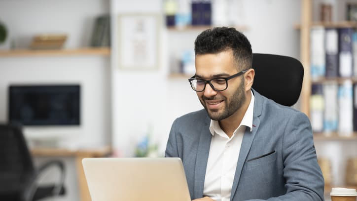 A man in glasses is using a laptop in his office.