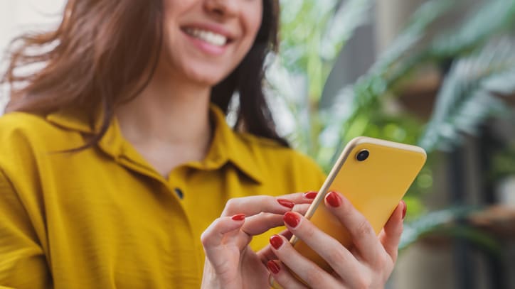 A woman is holding a yellow phone and smiling.