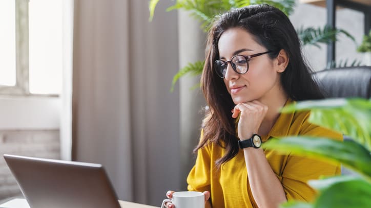 A woman sitting at her desk with a laptop and a cup of coffee.