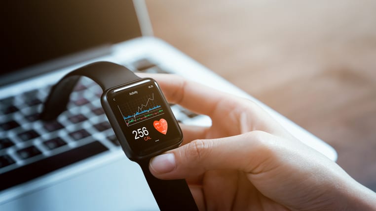 A person holding a smart watch in front of a laptop.