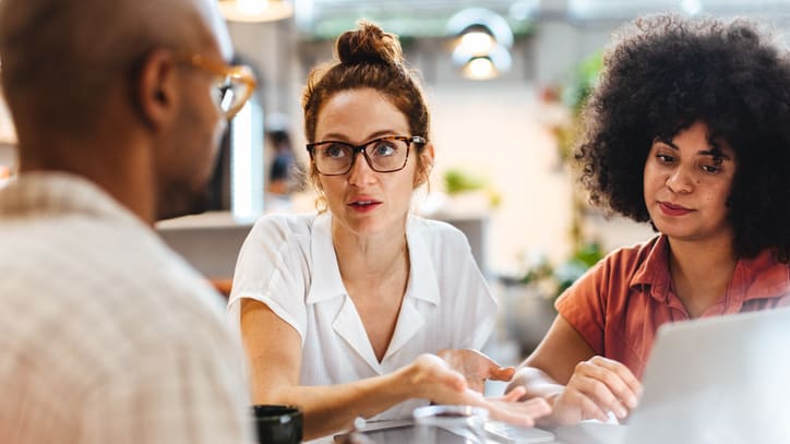 A group of people sitting around a table looking at a laptop.