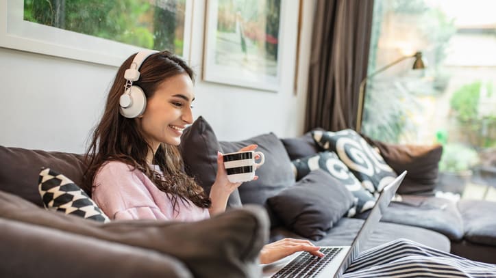 A woman sitting on a couch with headphones and a laptop.