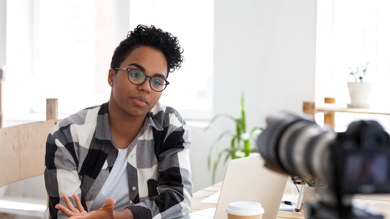 A woman is sitting at a table with a laptop and a camera.