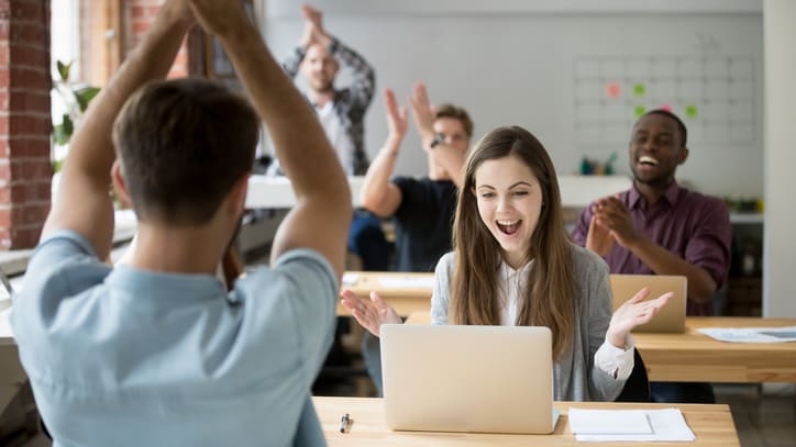 A group of people sitting at a desk and raising their hands in the air.