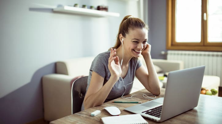 A woman is smiling while using a laptop at home.