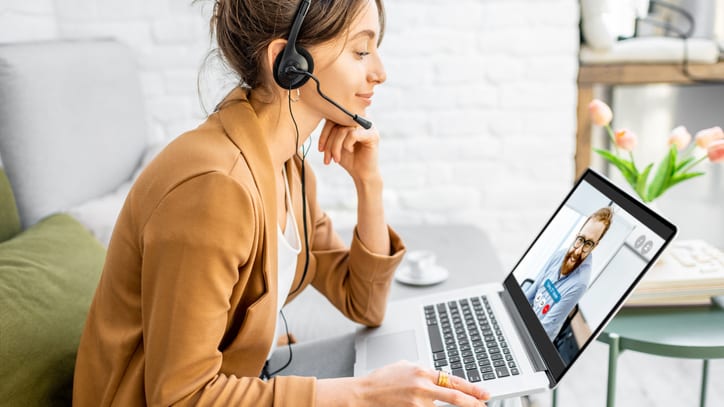 A woman wearing a headset is using a laptop while sitting on a couch.