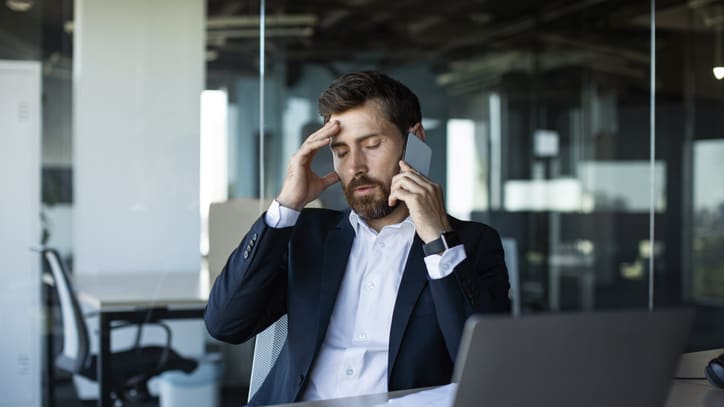 A businessman is talking on the phone while sitting at his desk.