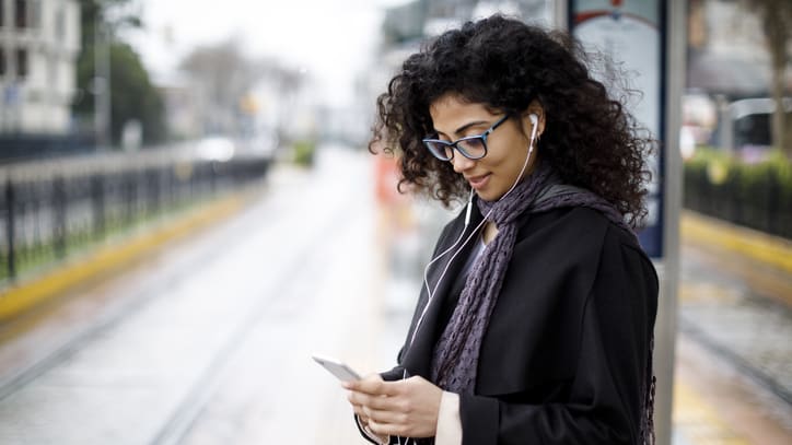 A woman is standing at a train station looking at her phone.