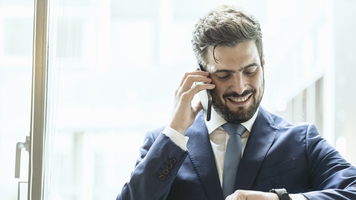 A man in a suit is talking on the phone while looking at his watch.