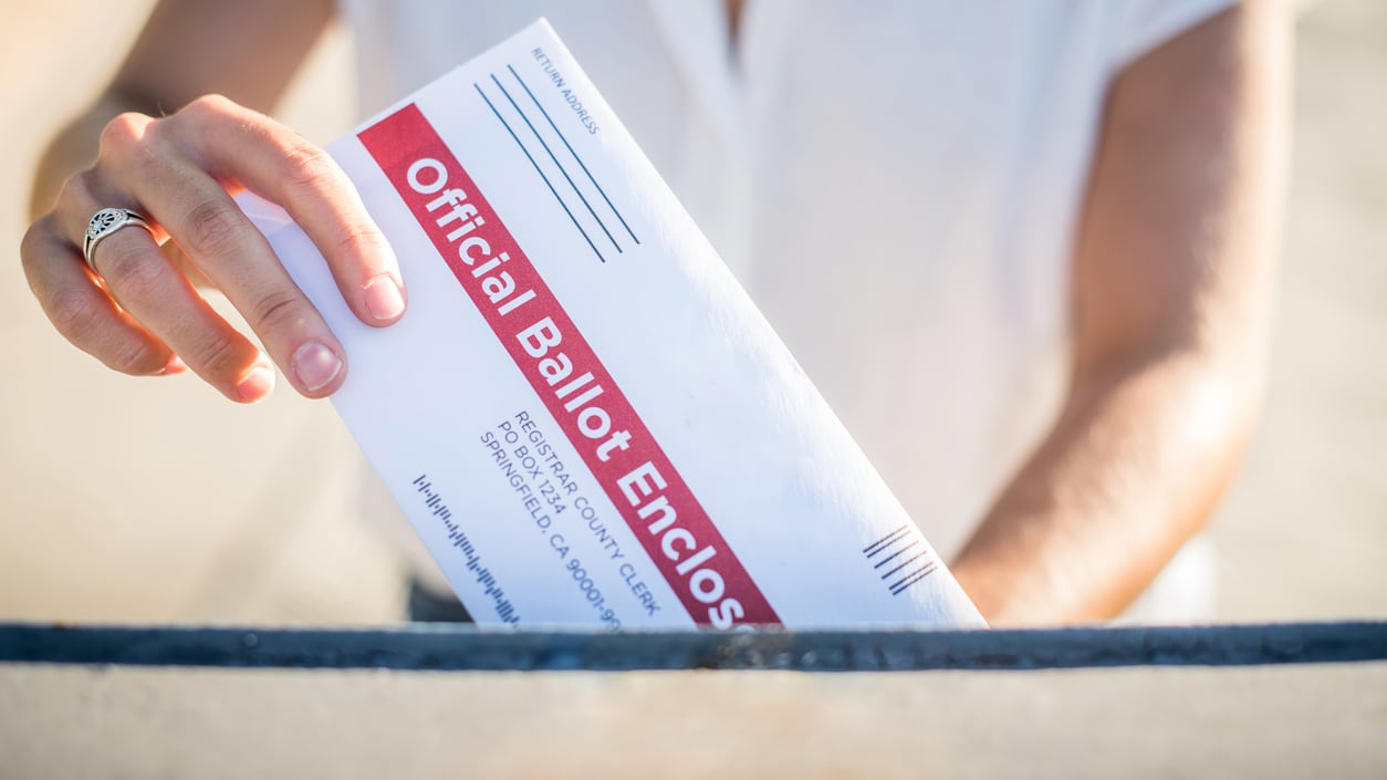 A woman is putting an envelope into a mailbox.