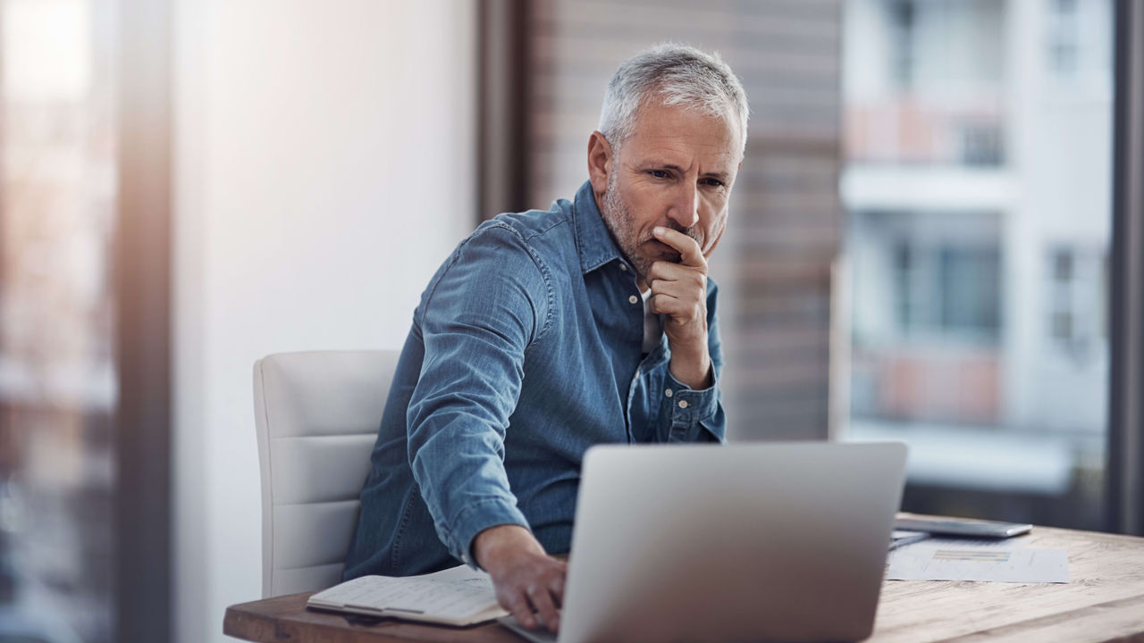 A man sitting at a desk looking at his laptop.