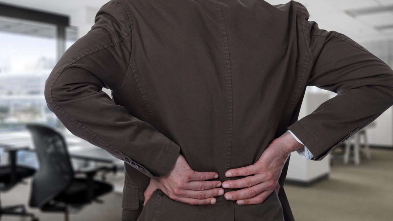 A man in a suit is holding his back in an office.