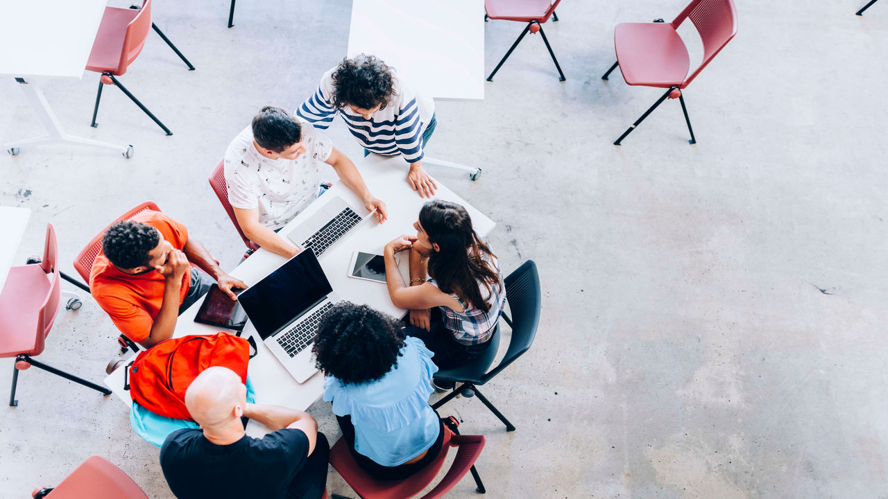 A group of people sitting around a table with laptops.