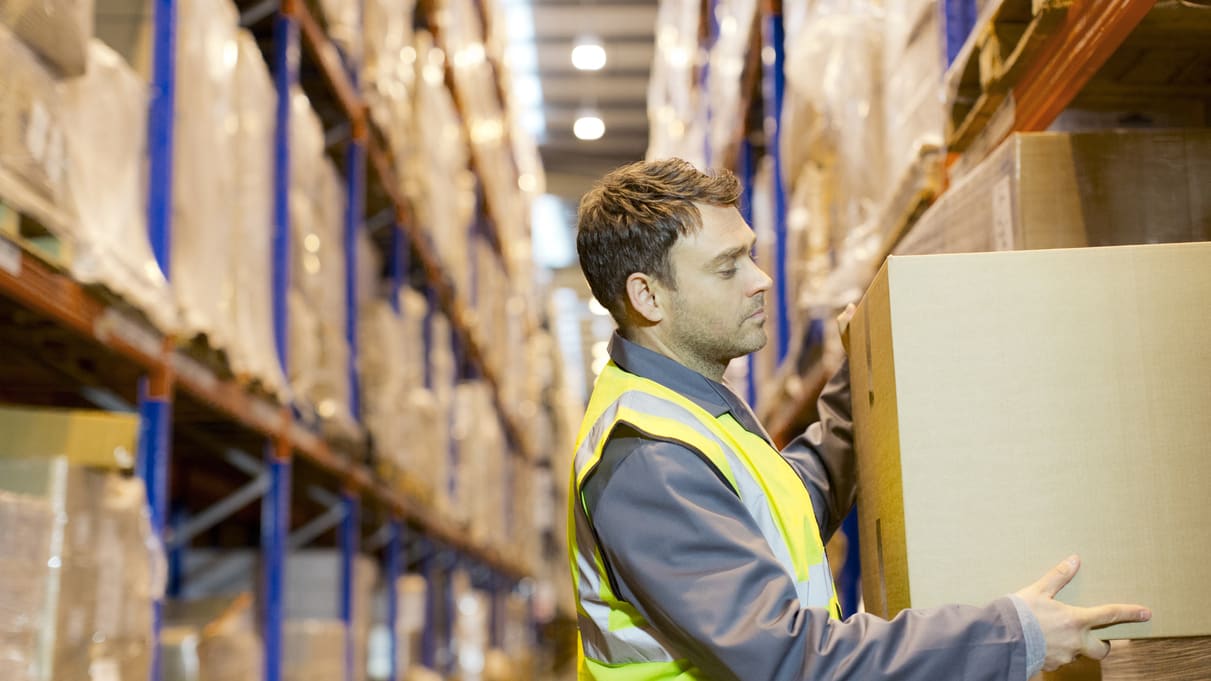 A warehouse worker picking up a box in a warehouse.
