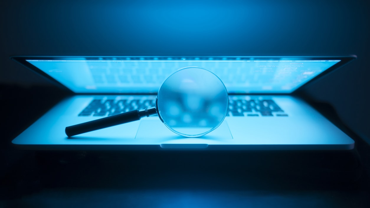 A laptop with a magnifying glass on it in the dark.