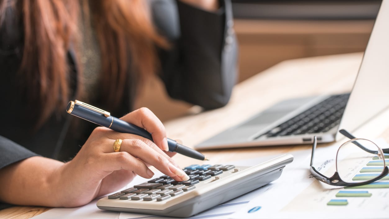 A woman is using a calculator while sitting at a desk.