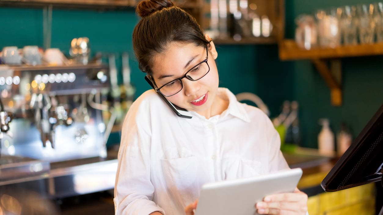 A woman in glasses is using a tablet in a coffee shop.