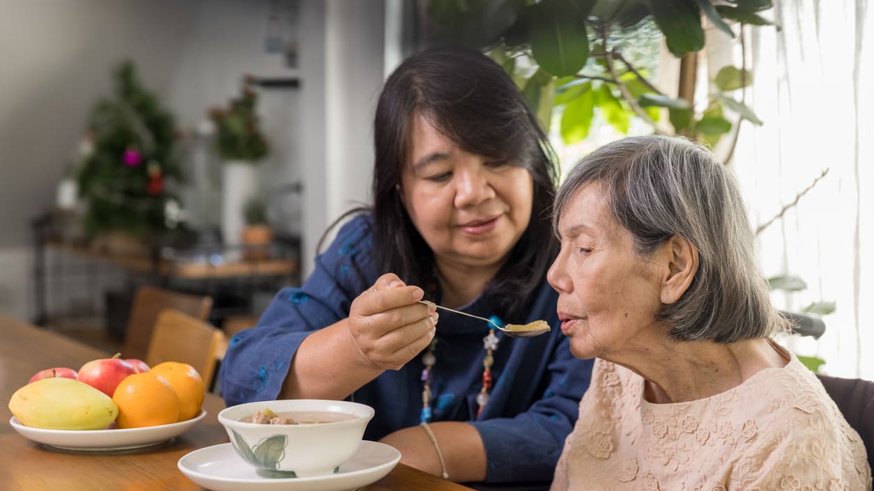 A woman is feeding an elderly woman at a table.