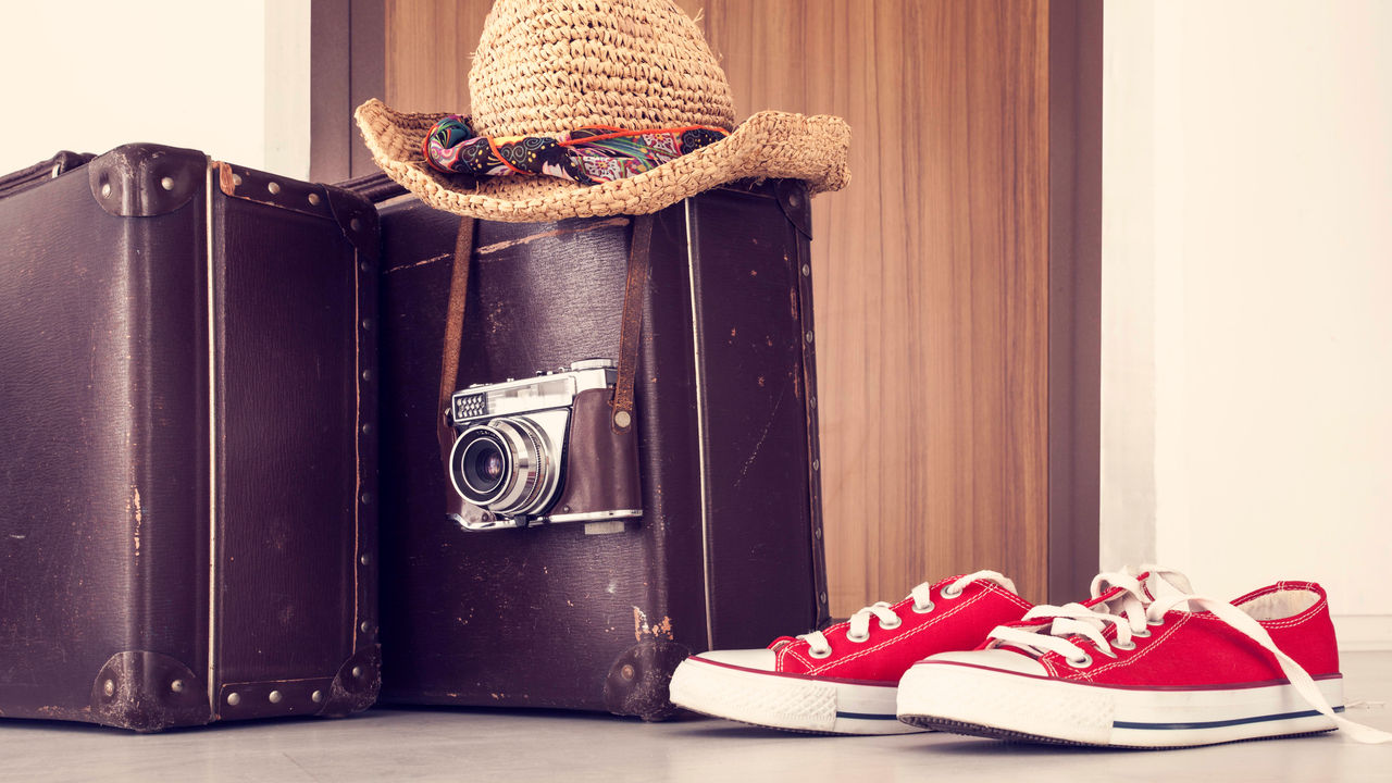 A brown suitcase with a hat and a pair of red shoes.