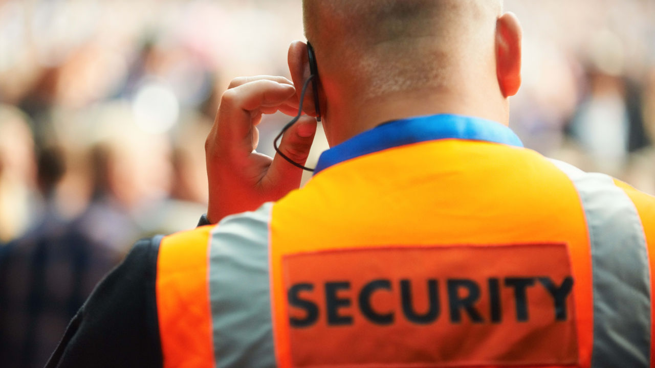 A security guard talking on the phone in front of a crowd.