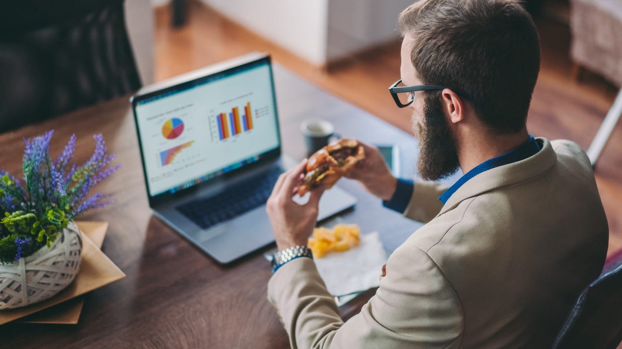 A businessman eating a hot dog while working on his laptop.