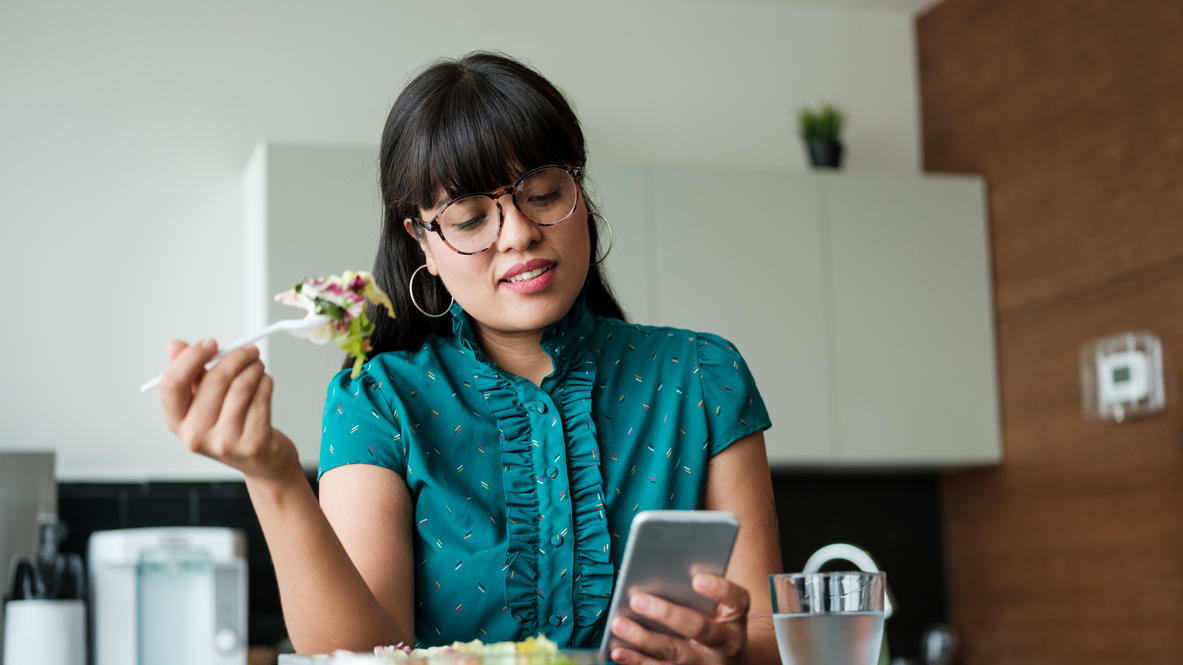 A woman eating a salad while looking at her phone.