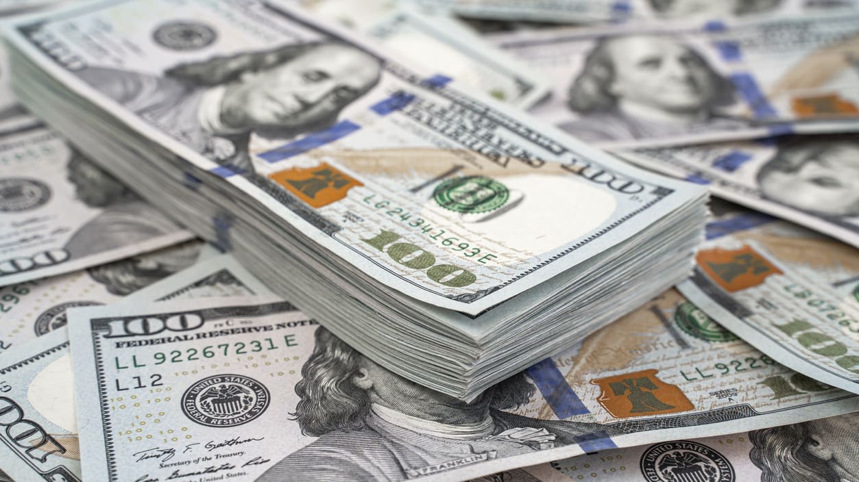 A pile of us dollar bills on a wooden table.