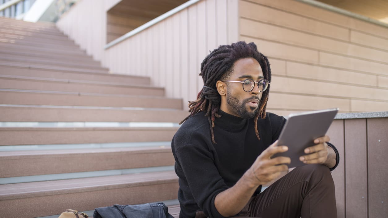 Young african american man sitting on the stairs using a tablet computer.