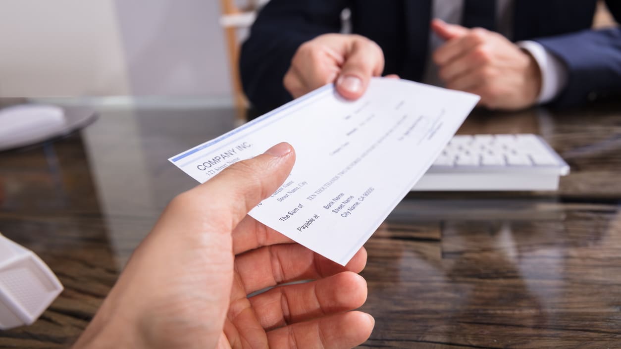 A businessman handing a check to another person at a desk.